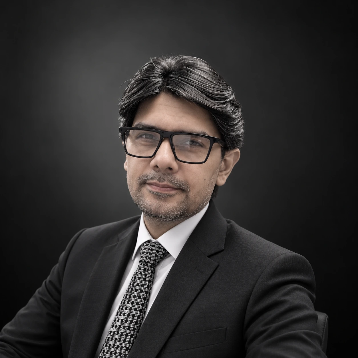 Portrait of Aasim Naseem in a dark suit against a charcoal background
